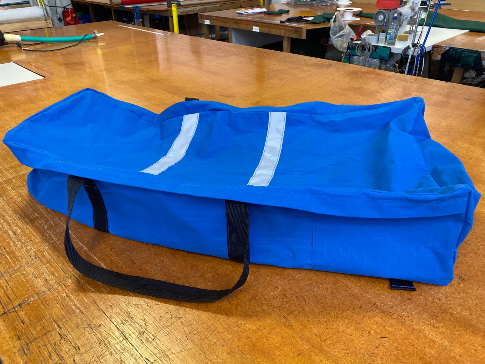 A finished blue bag with webbing handles on the cutting bench in the Levin workshop