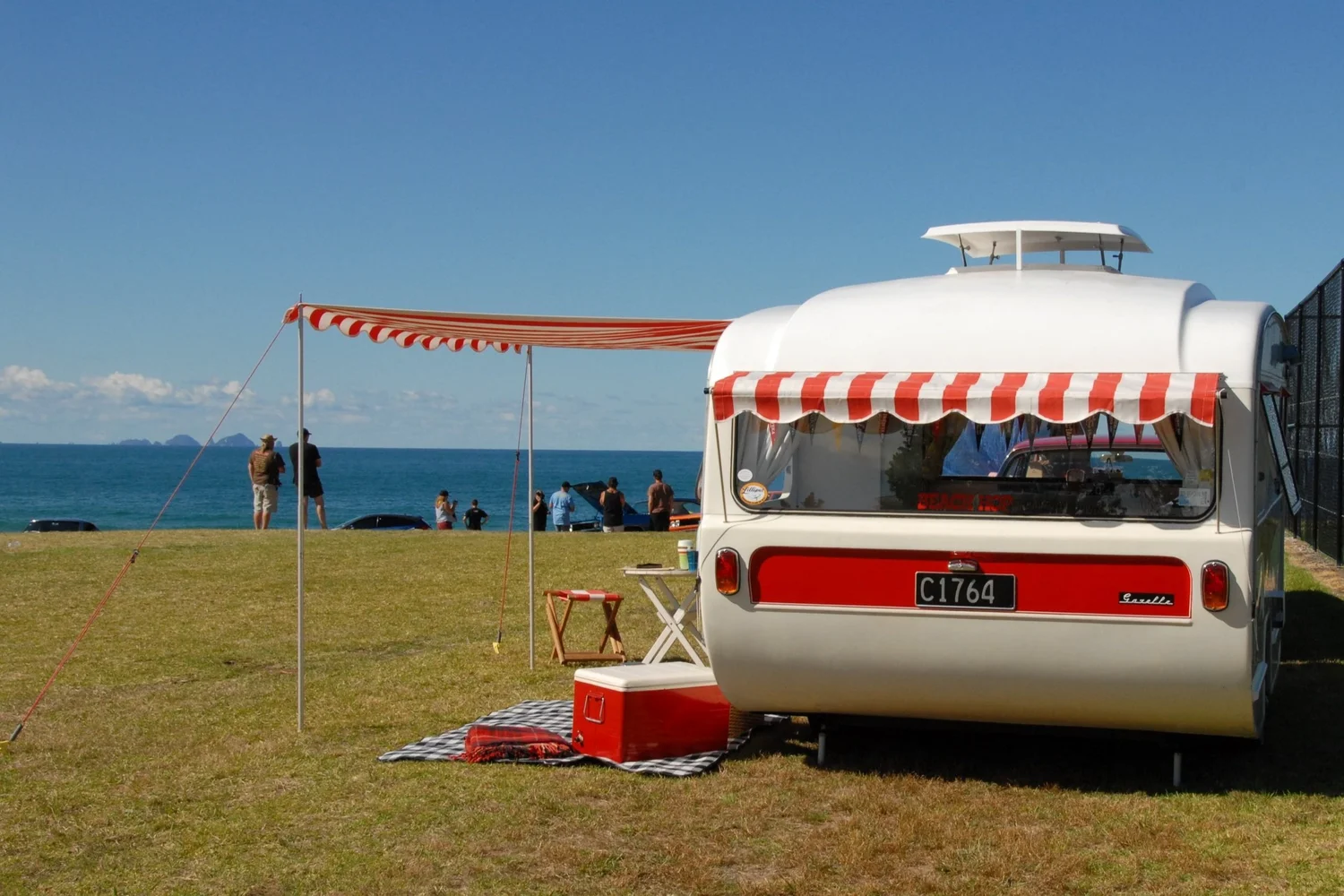 Vintage caravan with a red and white striped awning set up near the beach
