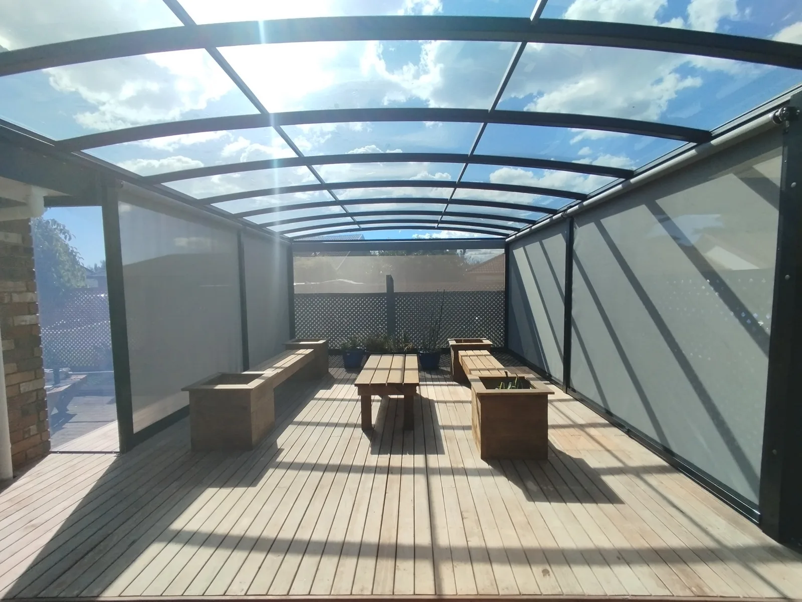 EasyTrack blinds down both sides of a long deck under a curved polycarbonate roof