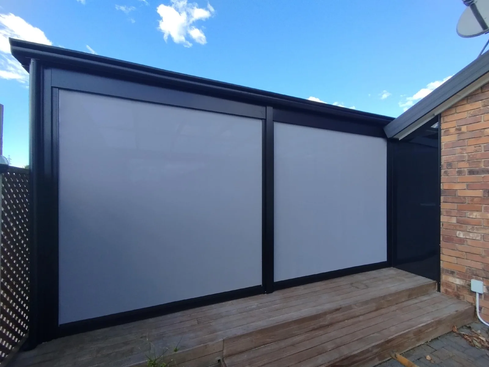 Two EasyTrack mesh blinds lowered across a covered deck beside a brick house