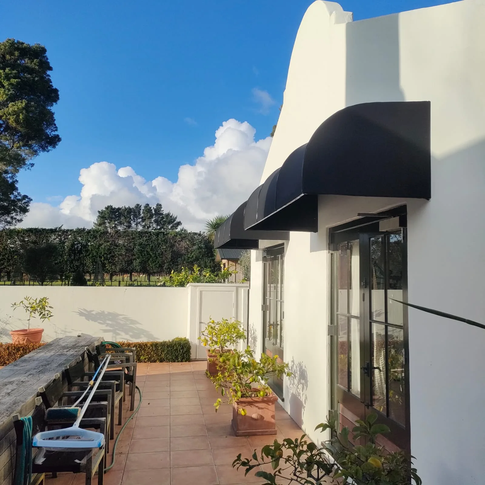 Fixed frame awnings shading a paved courtyard and outdoor table