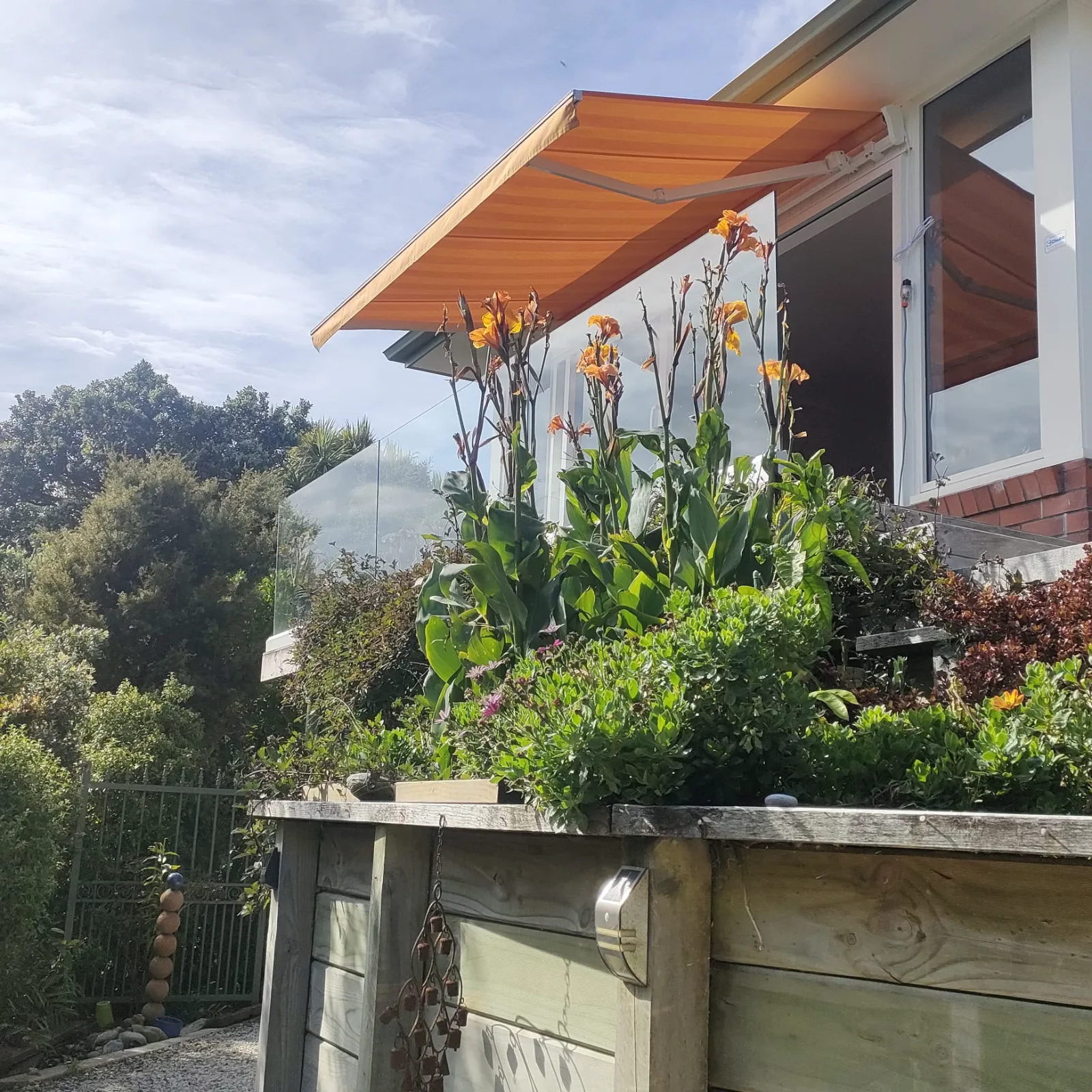 Orange lateral arm awning extended above a garden and raised planter