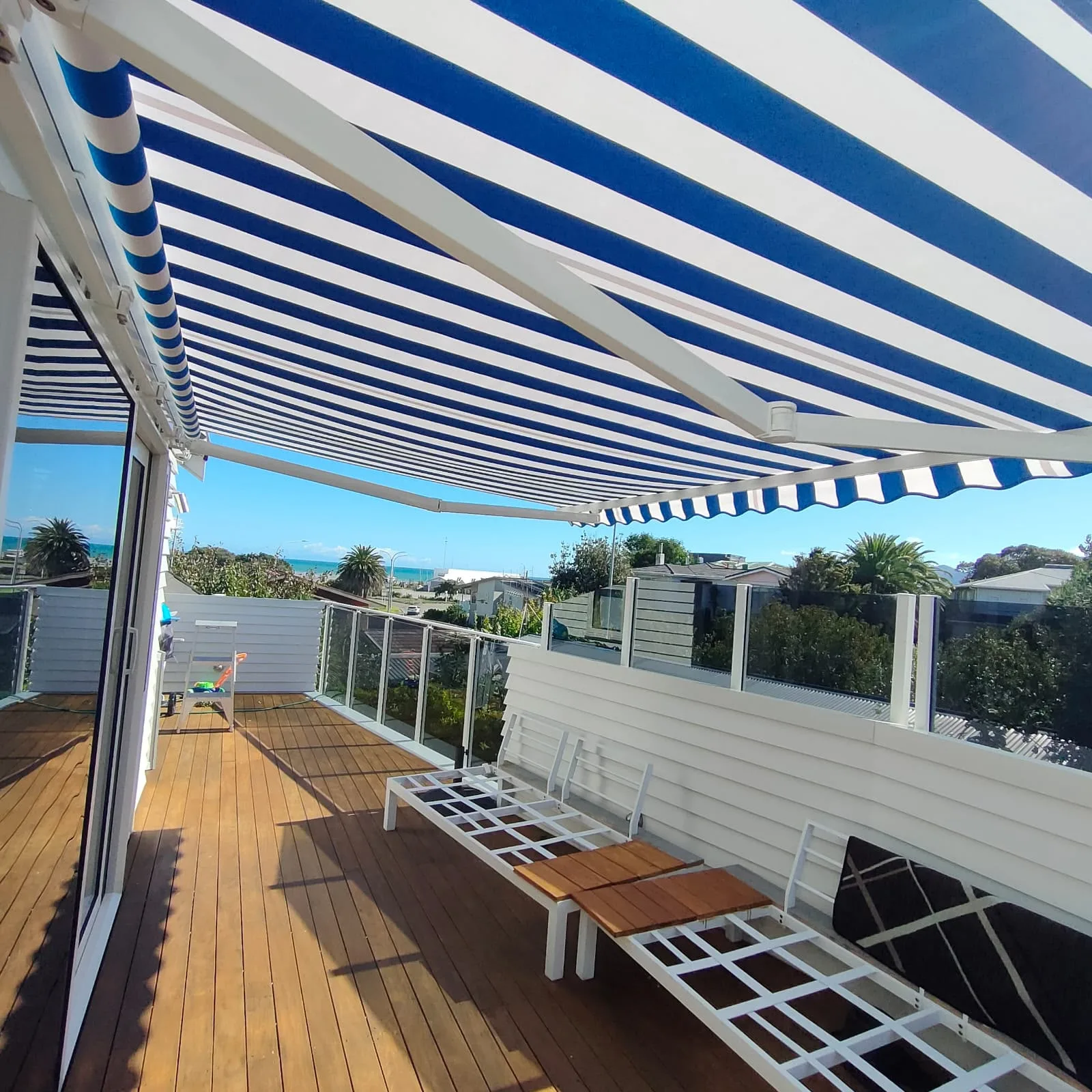 Blue and white striped lateral arm awning shading a coastal deck