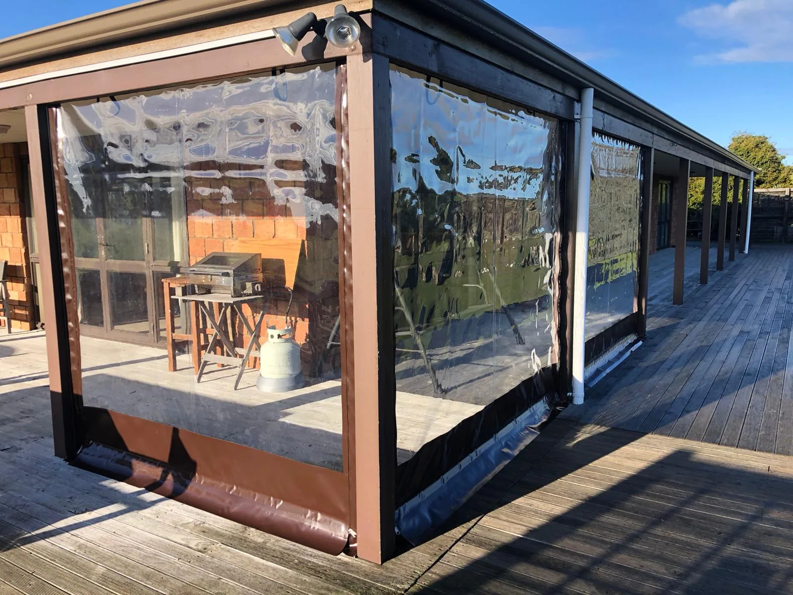 Clear PVC blinds with dark edging closing in the corner of a timber deck