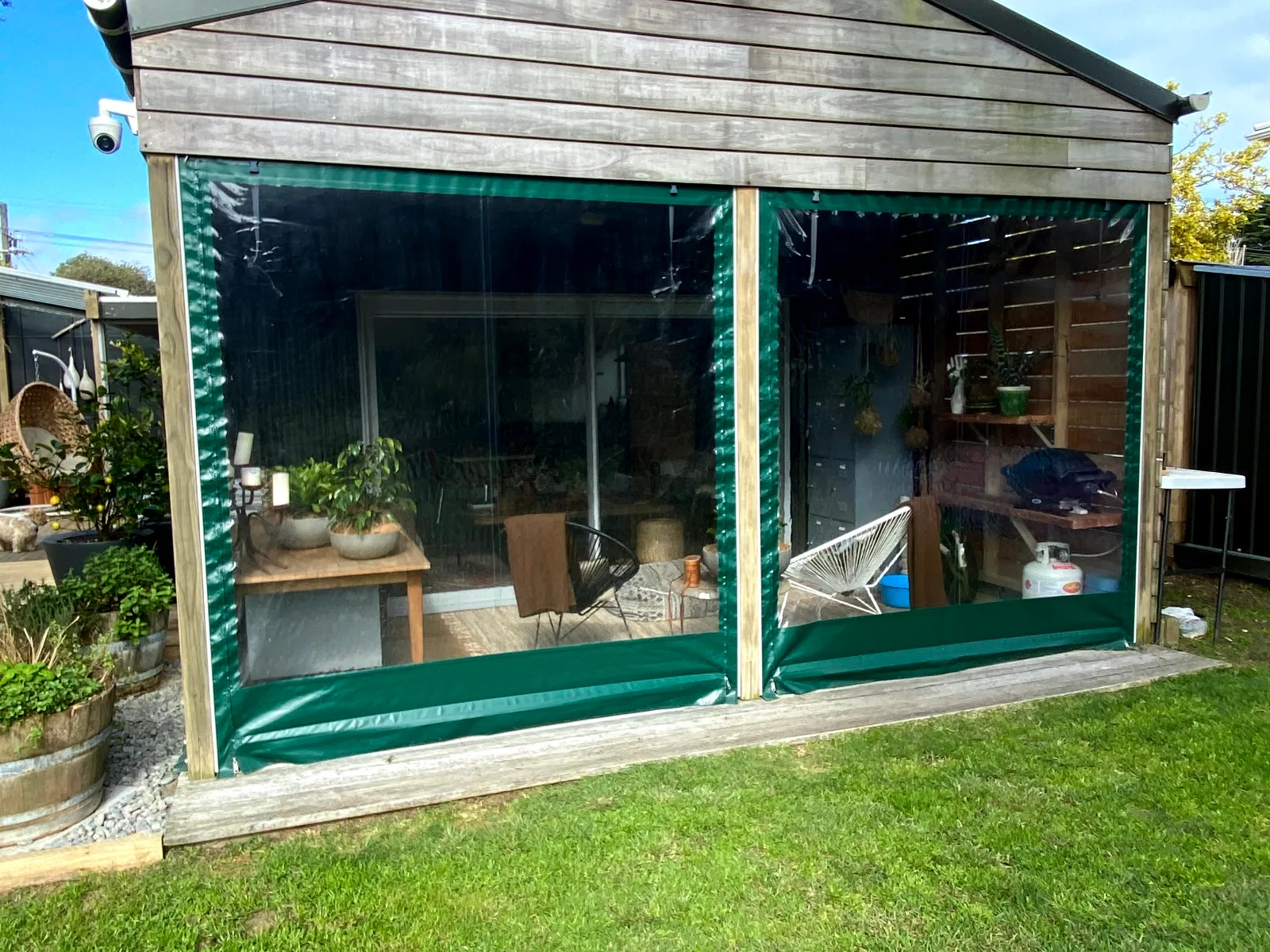 Clear PVC blinds with green edging closing in the front of a garden studio