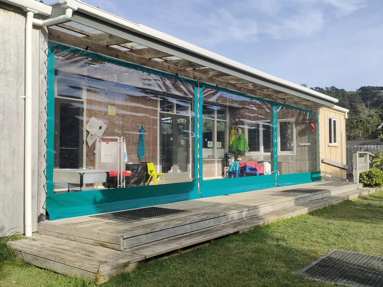 A long run of clear PVC blinds with teal edging along the front of a house
