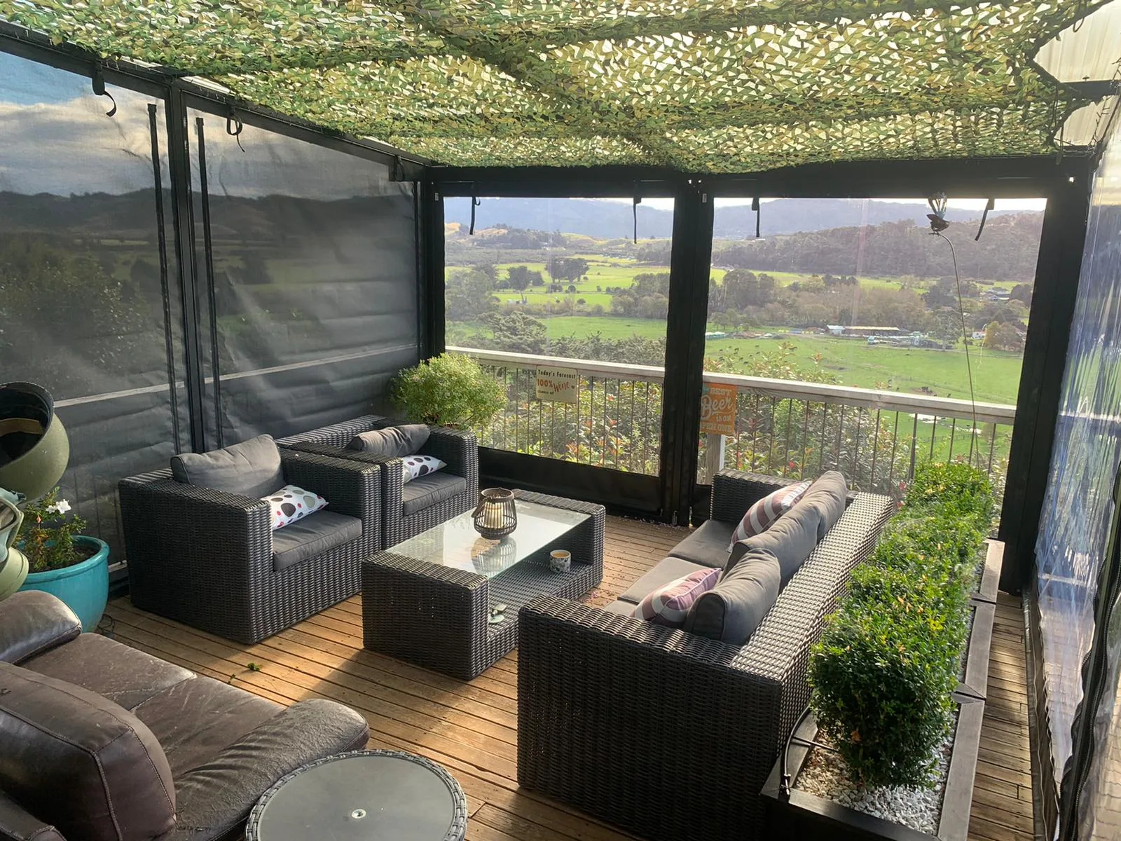 Outdoor lounge furniture behind blinds, looking out over a rural valley