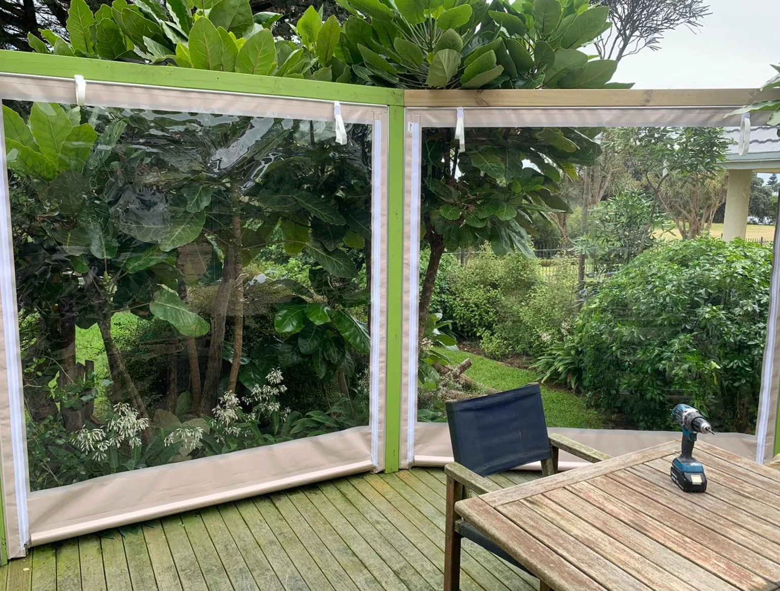 Clear zip-open PVC screens on a timber deck, with the garden visible through them