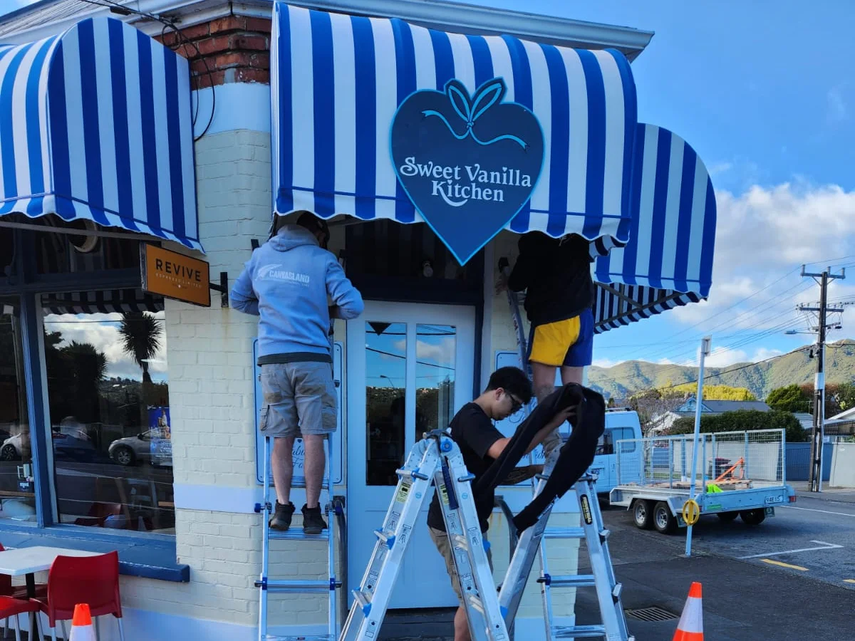 Canvasland team on ladders refitting a blue and white striped shop awning