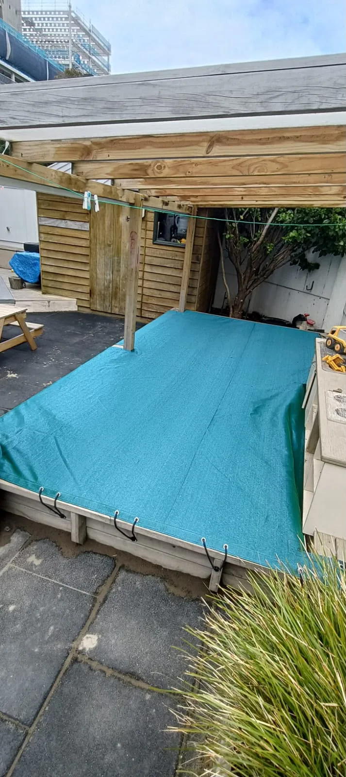Teal sandpit cover pulled over a raised sandpit on a childcare centre deck