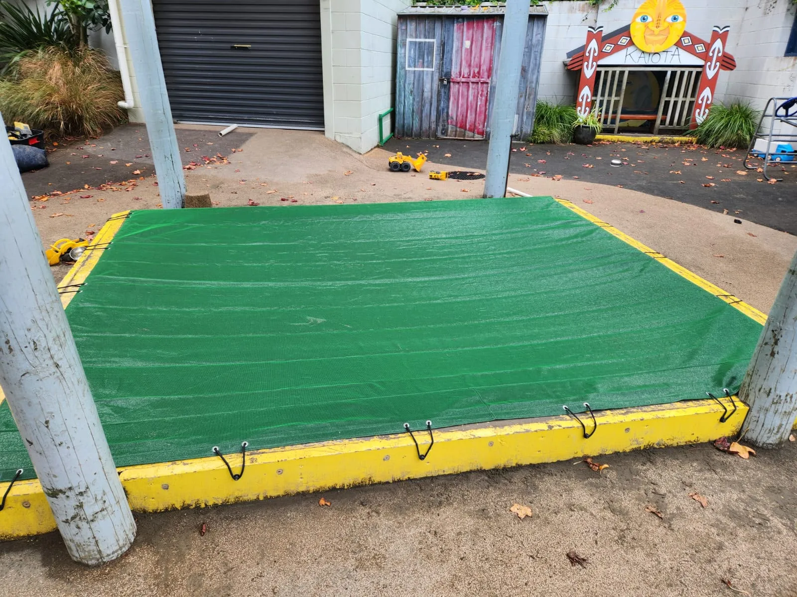 Green sandpit cover with a yellow edge, fitted over a school sandpit