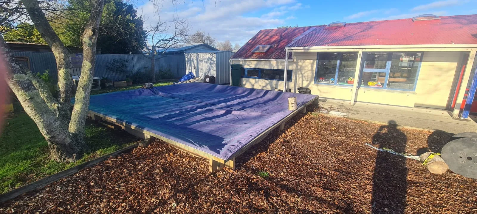 Purple sandpit cover fitted over a bark-edged sandpit