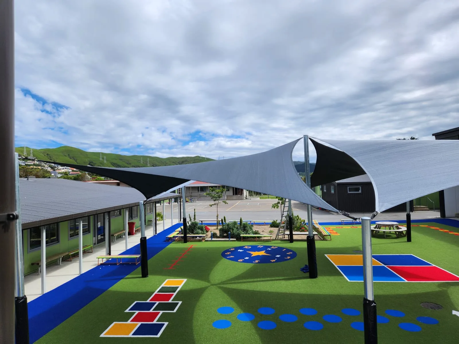 Shade sails over a school courtyard with hopscotch and number games painted on the turf