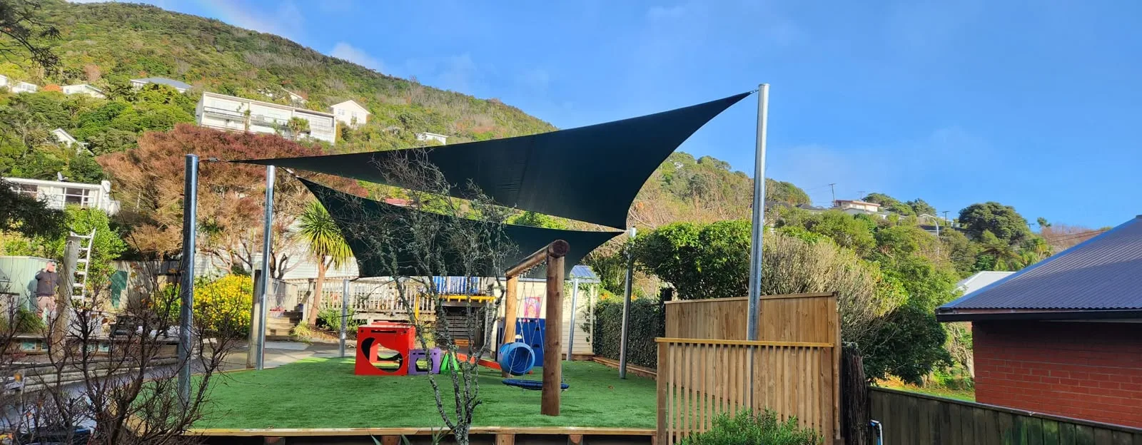 Navy shade sail over an early childhood centre playground and timber fort