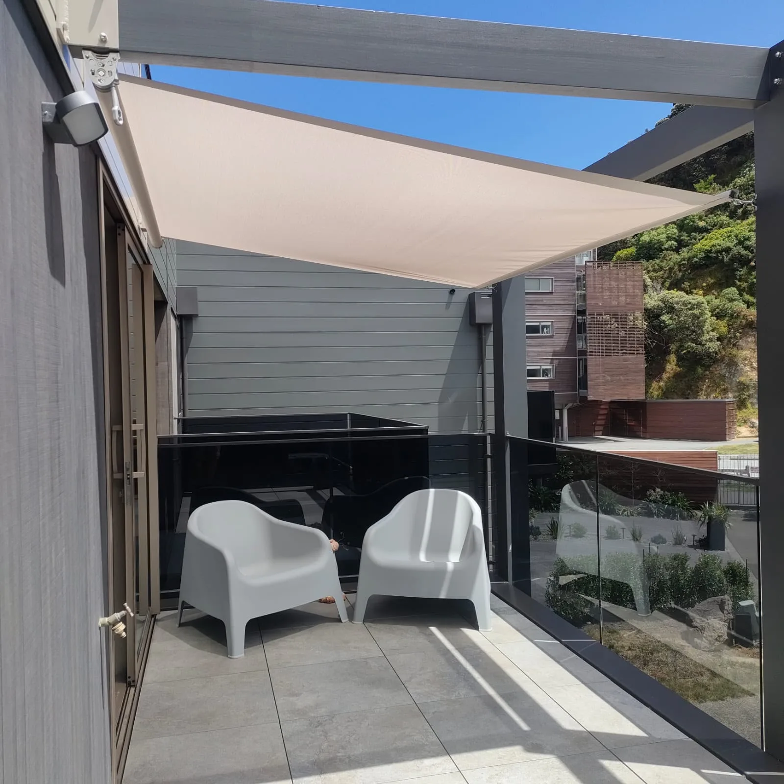 Cream shade sail over a sheltered courtyard with two armchairs