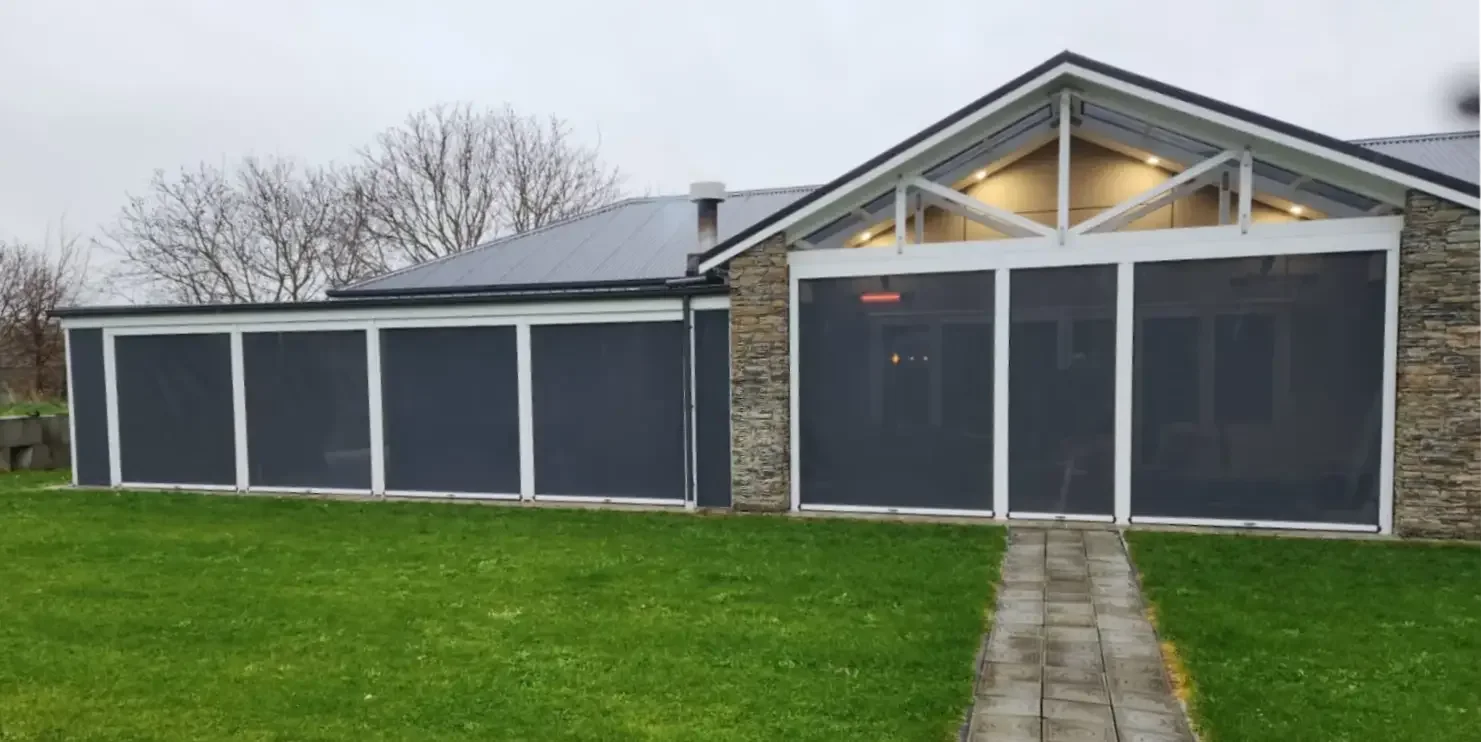 Ziptrak blinds enclosing the front of a home, lit from inside at dusk